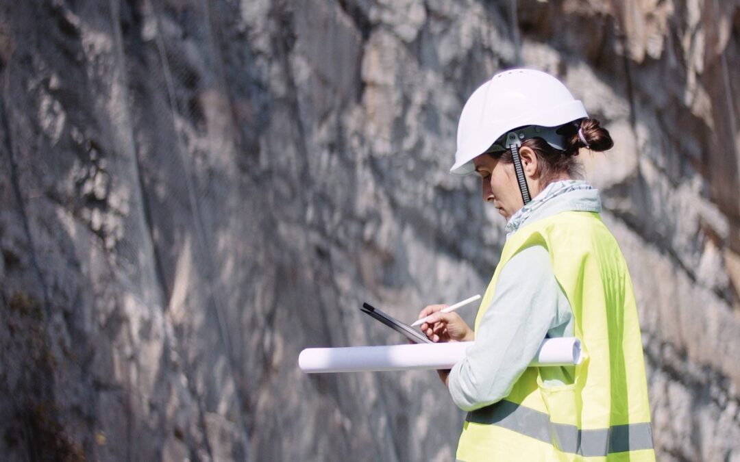 Female geologist holding clipboard, wearing hardhat, at job site at mine