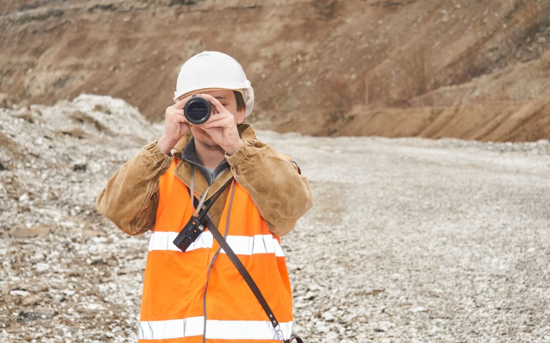 Geologist in hard hat holding survey scope surveying land in front of mine