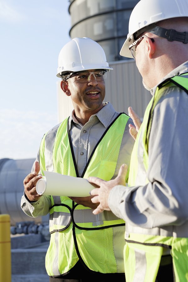 Contract Labor Two contracted mining workers discussing report in front of mining equipment