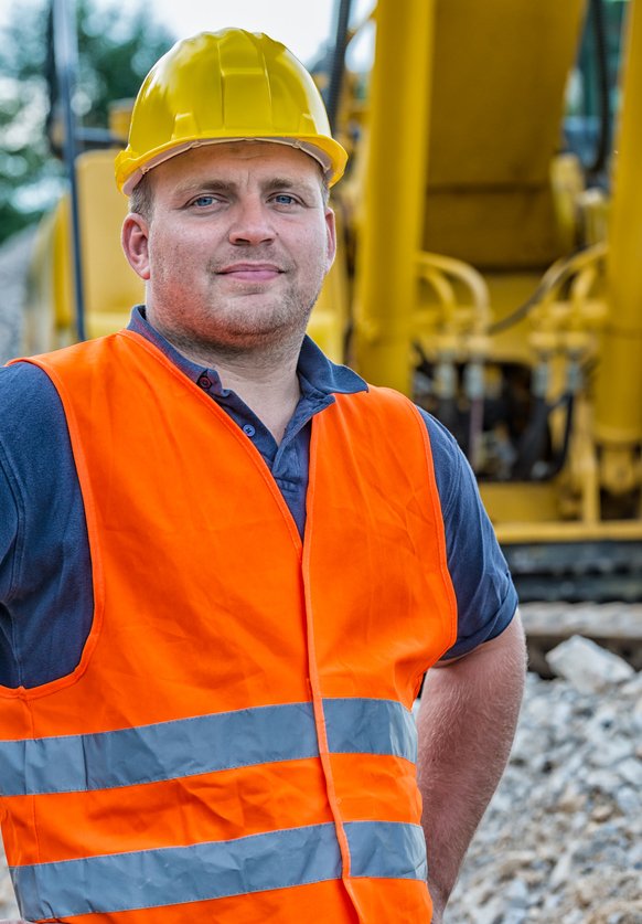Mining Consultant Male mining consultant in hard hat and vest at open pit mine in front of mining equipment